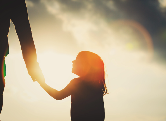 silhouette of little girl holding parent hand at sunset