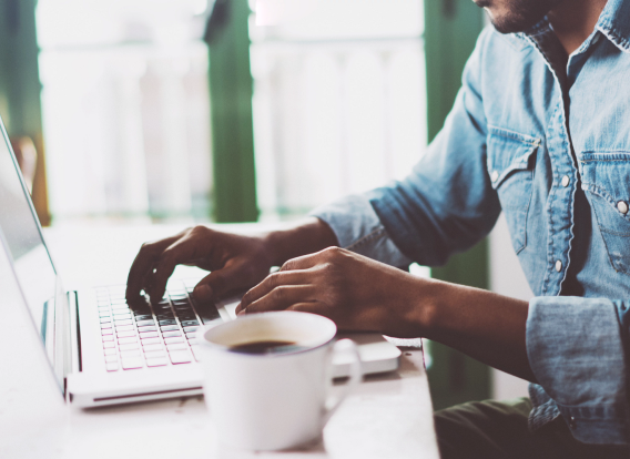 Smiling,Bearded,African,Man,Using,Laptop,At,Home,While,Sitting Smiling bearded African American male sing a laptop at home while sitting